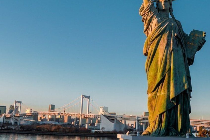 A statue of a woman holding a tablet, with a bridge and city skyline in the background. 5
