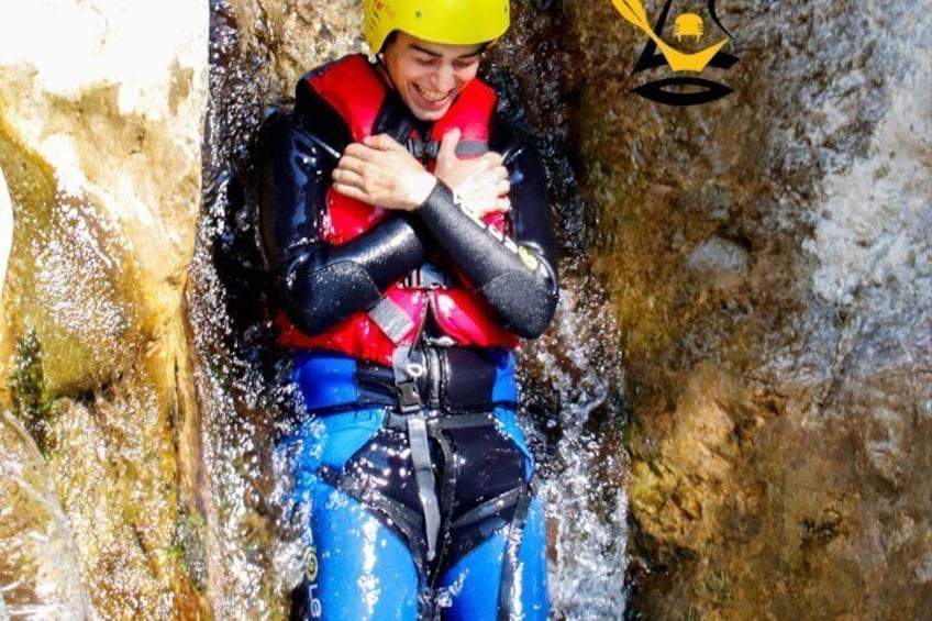 A person in a blue wetsuit and red life jacket, standing in a rocky cave. 4