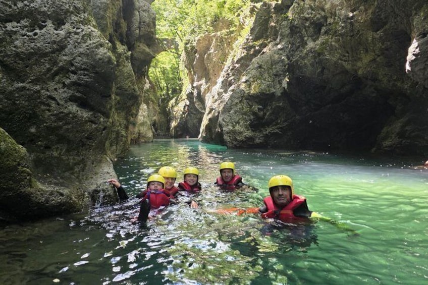 A group of people in a narrow canyon with clear water, wearing helmets and life jackets. 3
