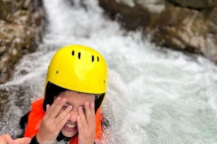 A person wearing a yellow helmet and an orange life jacket, partially submerged in a flowing river. 1