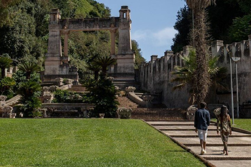 A historical stone structure with inscriptions, surrounded by a well-maintained garden with palm trees. 2