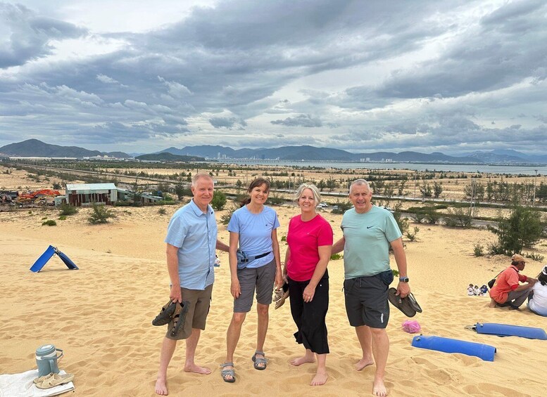 A group of people standing on a sandy beach with a desert landscape and mountains in the background. 5