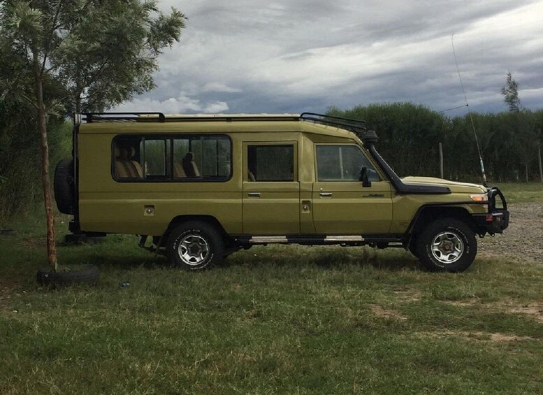 A green off-road vehicle parked on a grassy field with trees in the background. 4