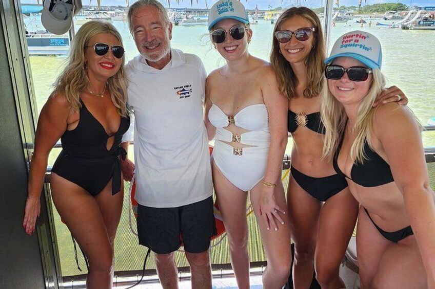 Un grupo de personas en un bote, con trajes de baño y sombreros, y un puerto deportivo al fondo. 4