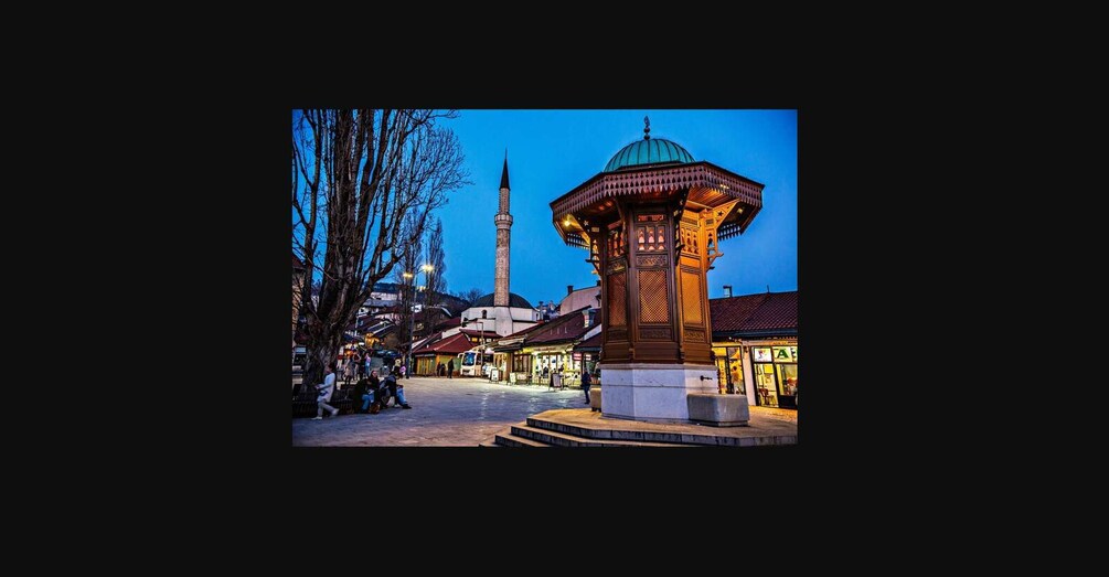 A night scene with a traditional wooden gazebo, a mosque with a minaret, and a tree-lined square. 5