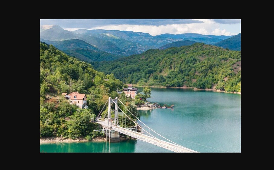 A suspension bridge over a calm lake surrounded by lush green hills and mountains. 2