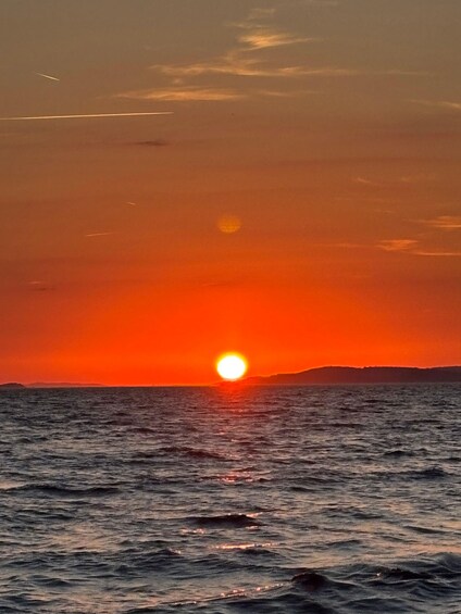 A sunset over the ocean with a visible sun and distant land. 3