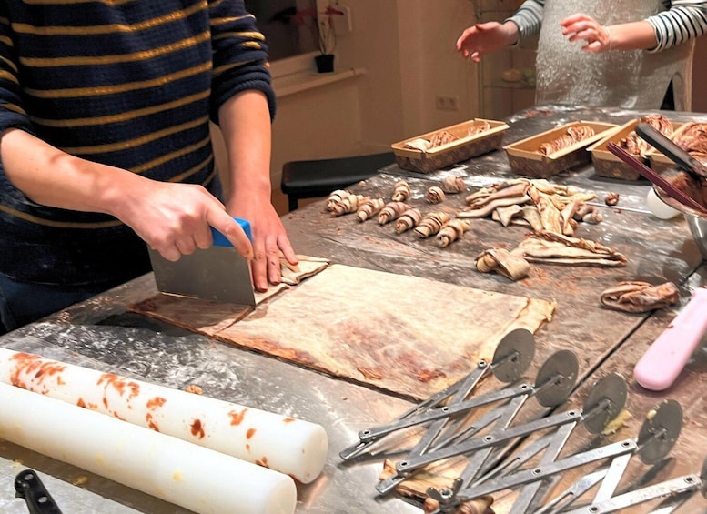 A person cutting dough on a marble countertop with various tools and dough pieces scattered around. 5