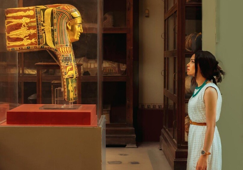 A museum interior with a glass display case containing a golden Egyptian sarcophagus. 4