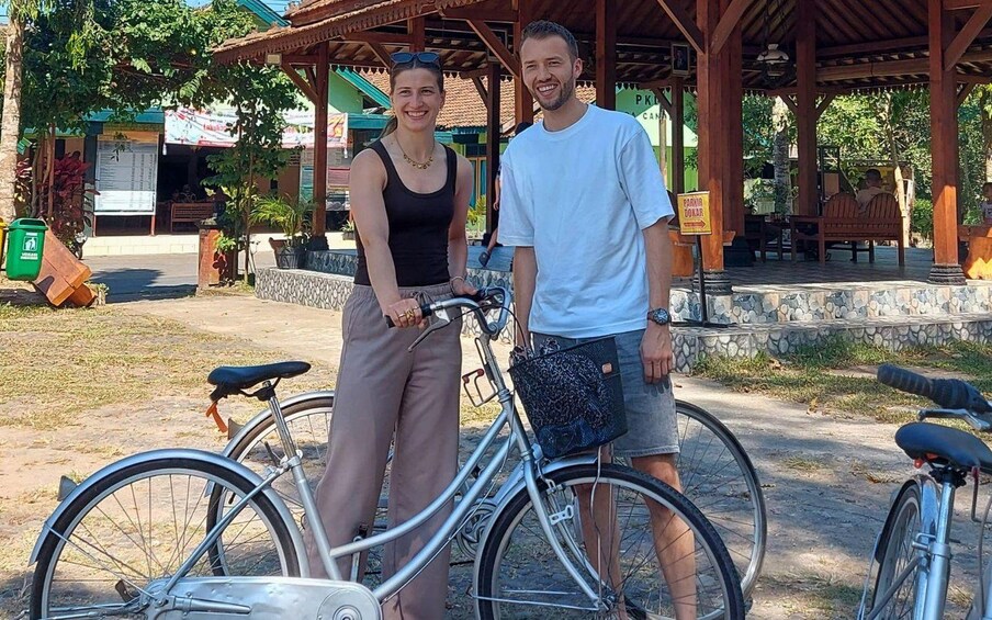Two people standing next to bicycles in a park with a wooden pavilion and a sign that reads 'PARKING DOLLAR'. 2