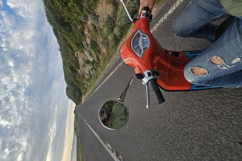 En röd scooter på en asfalterad väg, och en person som bär trasiga jeans. 5