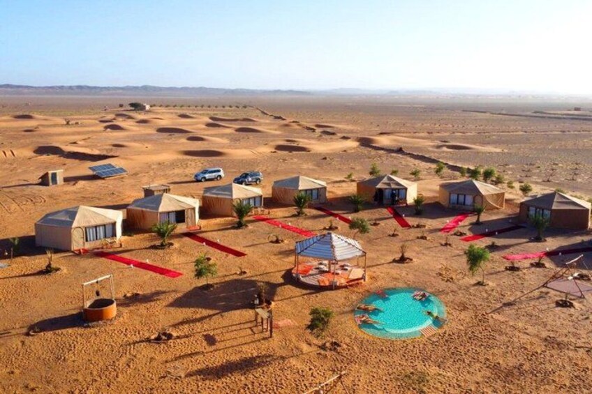 A desert resort with multiple tents, a swimming pool, and solar panels. 2