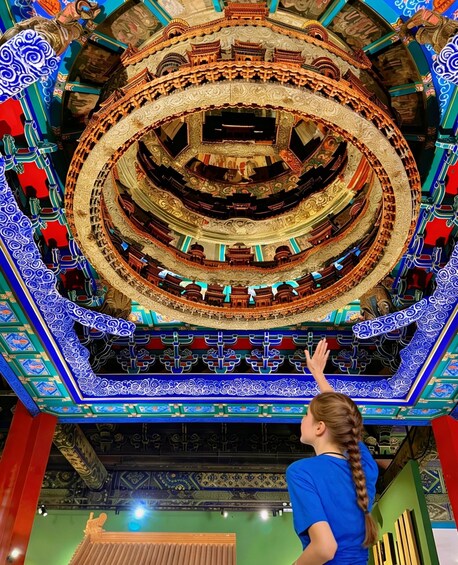 A person observing a multi-tiered, intricately decorated ceiling with traditional architectural elements. 2