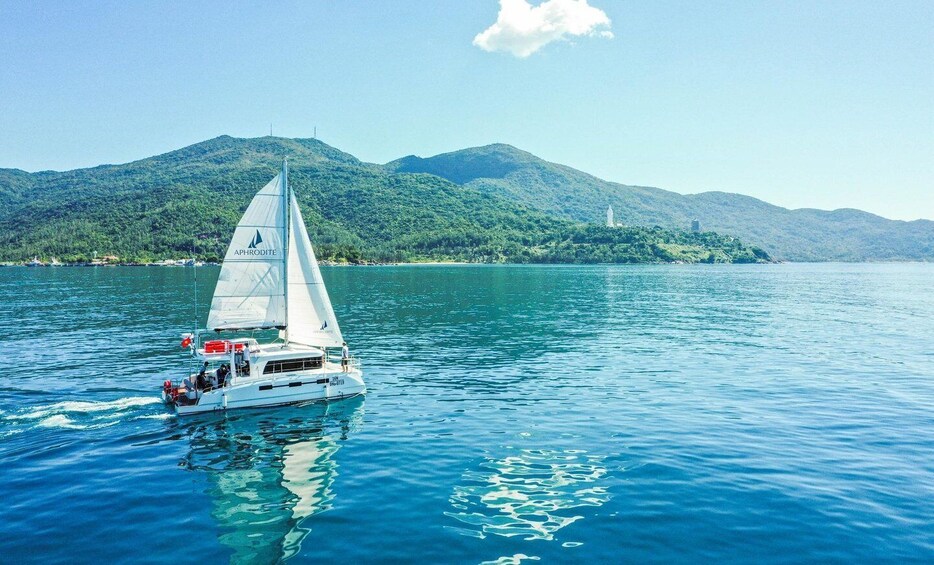 A sailboat named 'APHRODITE' on calm waters with a mountainous landscape in the background. 1