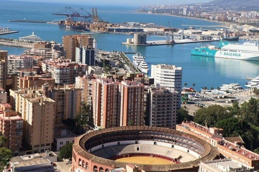 A bullring surrounded by urban buildings and a port with ships. 3