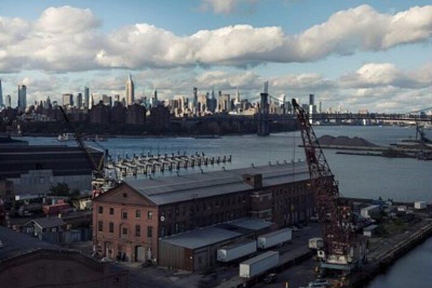 Ett industriområde vid vattnet med lagerbyggnader, en kran och en stadsbild i bakgrunden. 4
