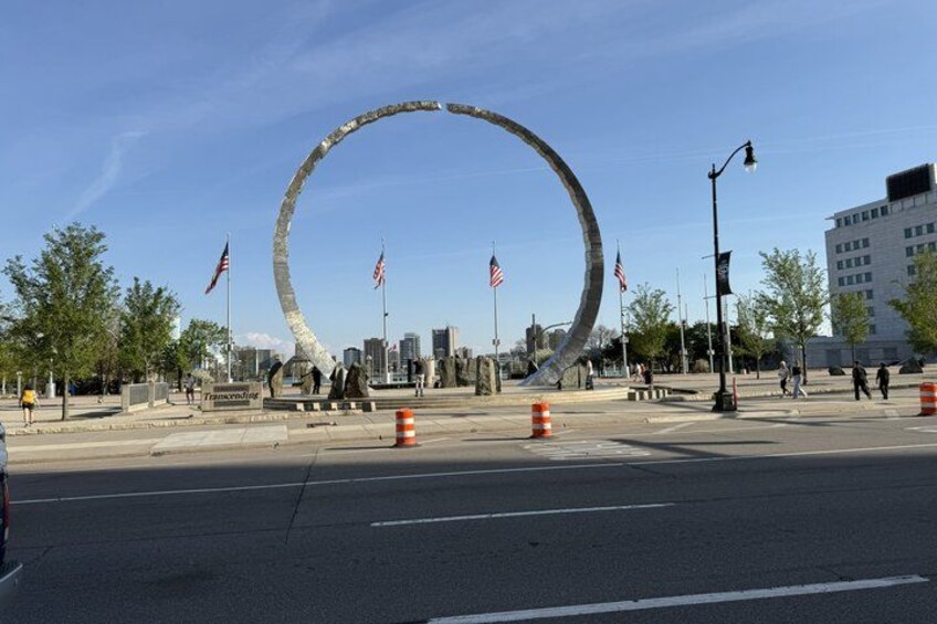 Ett runt monument med amerikanska flaggor, en stadsbild i bakgrunden och trafikkoner på vägen. 2