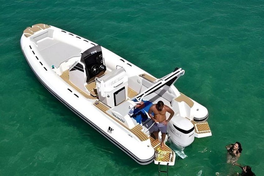 A white motorboat with a wooden deck, a person standing at the bow, and another person in the water. 5