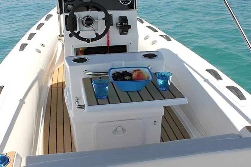 A boat's deck with a steering wheel, a small table with a bowl of fruit, and two glasses. 2