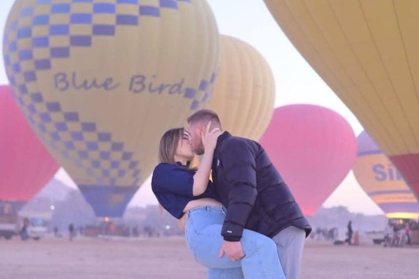 A couple embracing in front of hot air balloons with 'Blue Bird' written on one. 5