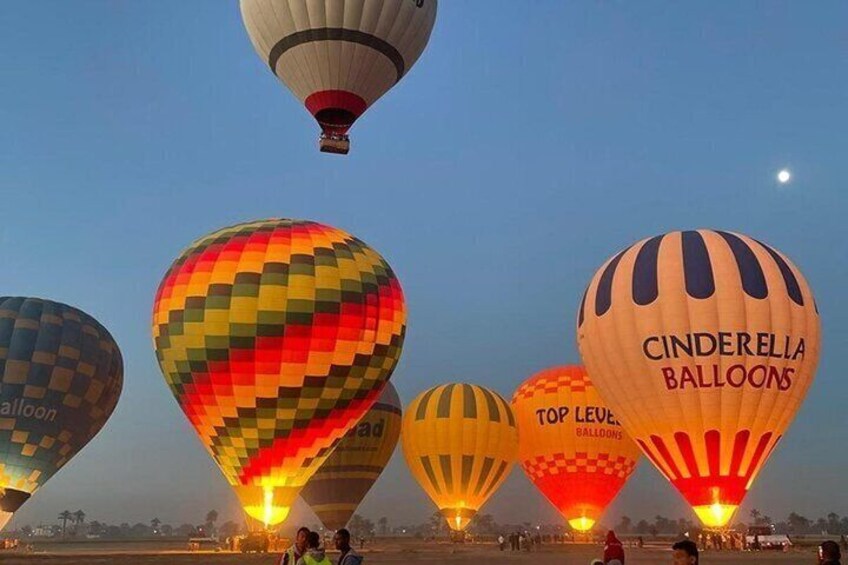 A line of colorful hot air balloons at dusk with visible company names. 1