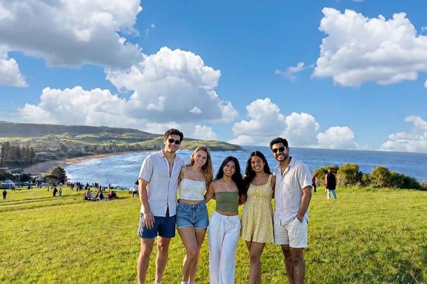 A group of people standing on a grassy hill with a view of the ocean and hills in the background. 1