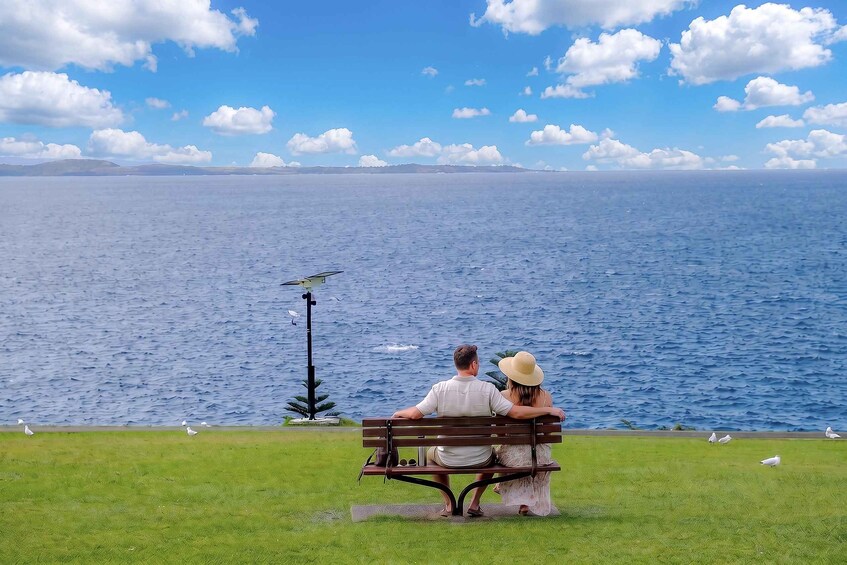 A couple sitting on a bench overlooking a body of water with birds and a lamp post in the foreground. 5
