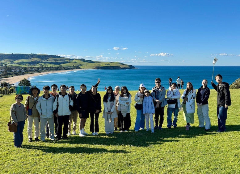 A group of people standing on a grassy hill overlooking a beach and ocean. 2