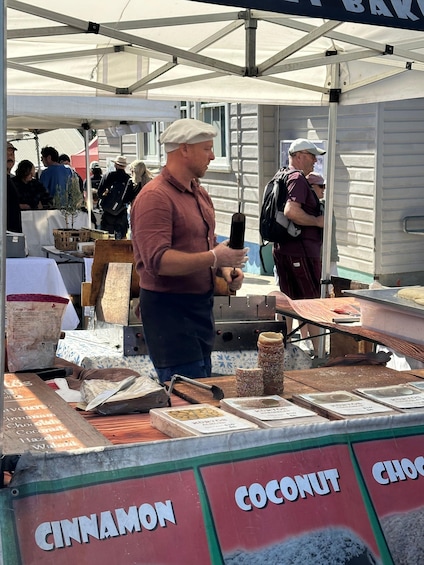 A person at a food stall with a sign indicating flavors like cinnamon, coconut, and chocolate. 3