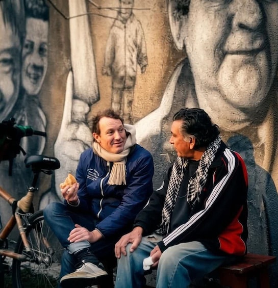 Two people sitting on a bench in front of a mural. 4