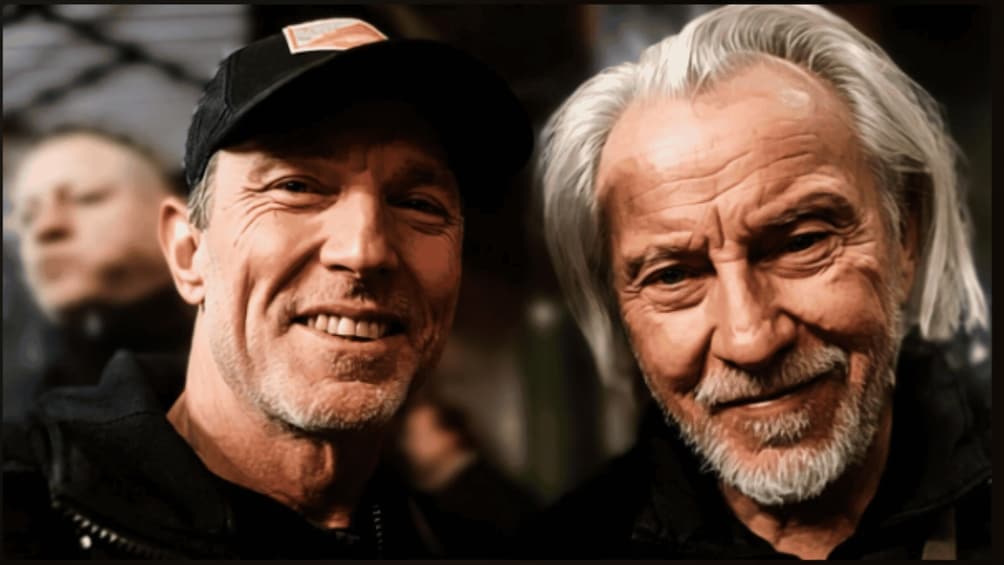 Two men in close proximity, one wearing a cap. 2
