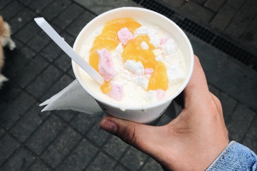Une personne tenant une tasse avec une paille, contenant un dessert garni de décorations orange et rose. 4