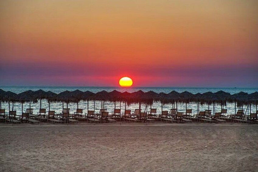Een zonsondergang boven een strand met rijen strandstoelen en parasols. 2