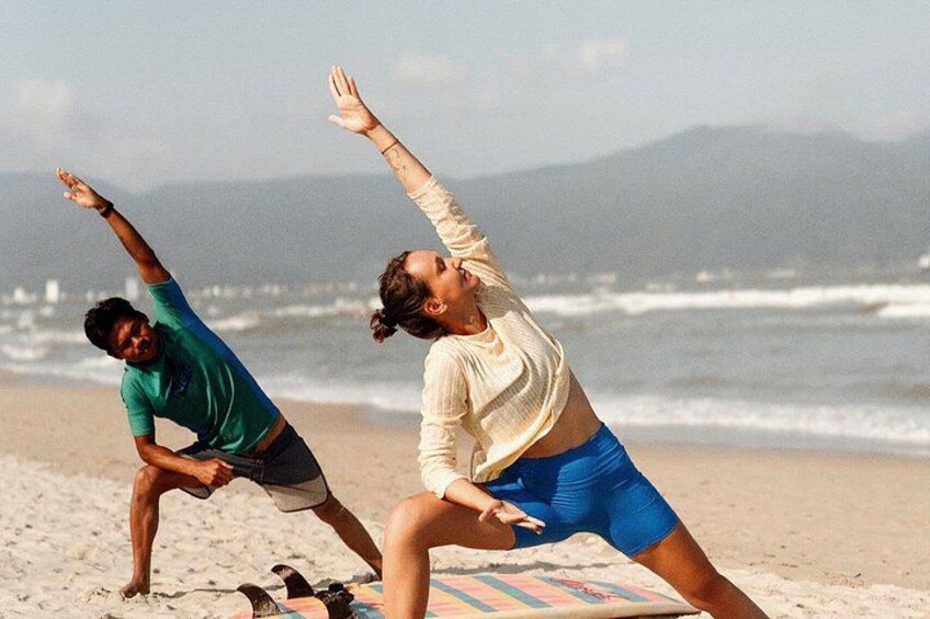 Twee mensen doen een yoga-houding op het strand, met golven in de verte. 1