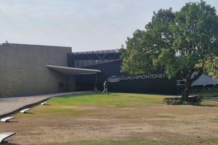 A building with a Guachimontones logo, a grassy area, and a tree. 1