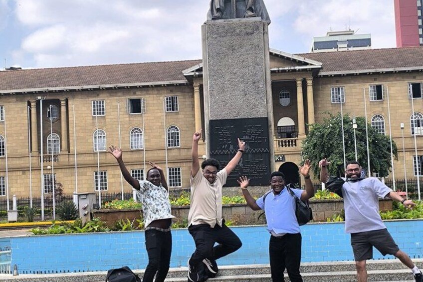 Quatre personnes posent devant un bâtiment surmonté d’un grand monument. 4