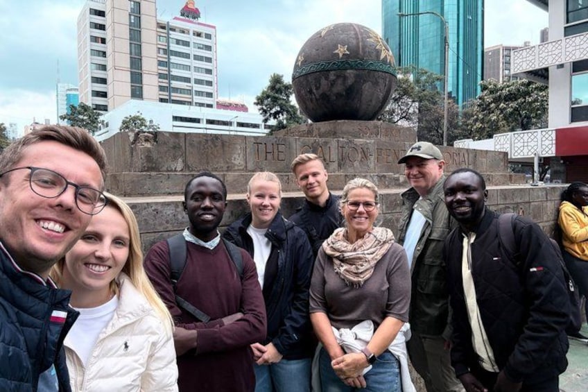 Un groupe de personnes se tient devant un monument sur lequel figure un globe terrestre et une inscription. 5