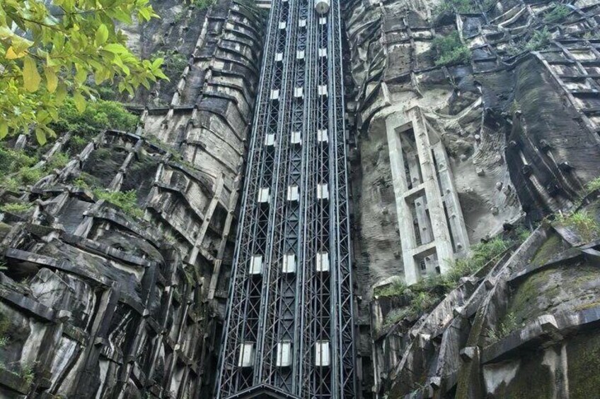 A steep, narrow staircase carved into a rocky cliffside, with a metal safety railing and a small window at the top. 5