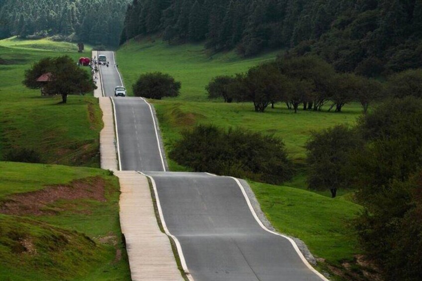 A winding road through a hilly landscape with trees and a distant building. 3