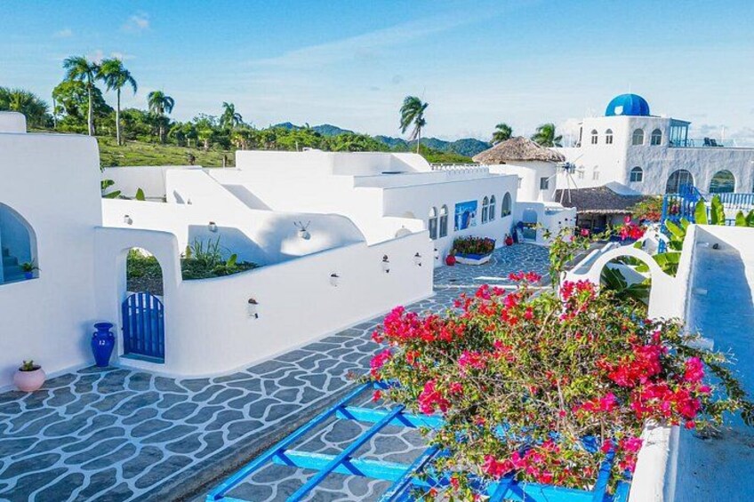 Un edificio blanco con detalles azules, una reja azul y flores de buganvilla rosadas. 2