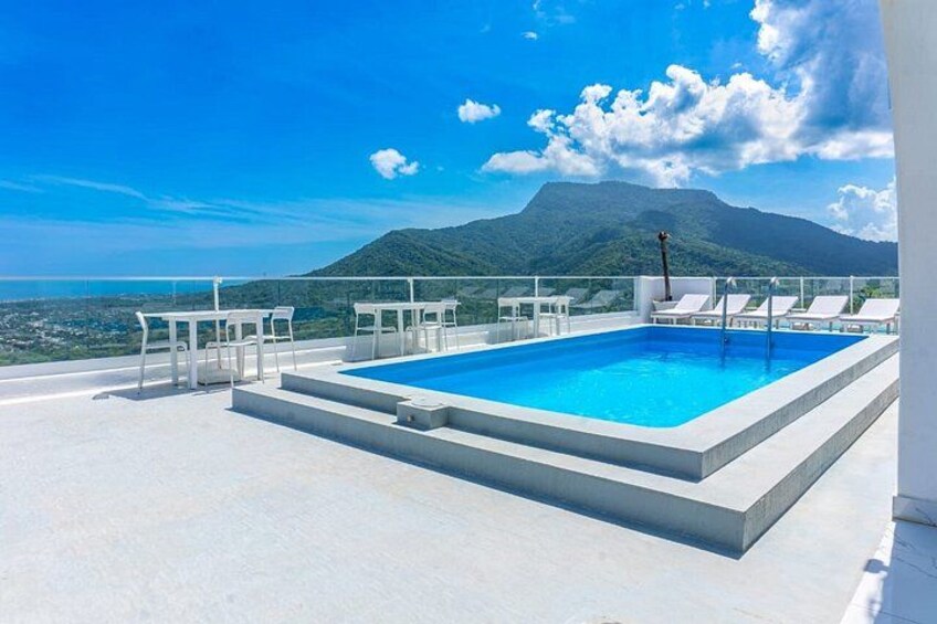 Una piscina en la azotea con sillas y mesas blancas, con vistas a un paisaje montañoso. 3