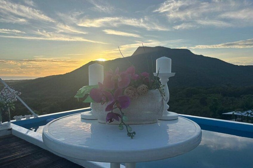 Una mesa blanca con un jarrón de flores y velas en un balcón con vistas a un paisaje montañoso al atardecer. 5