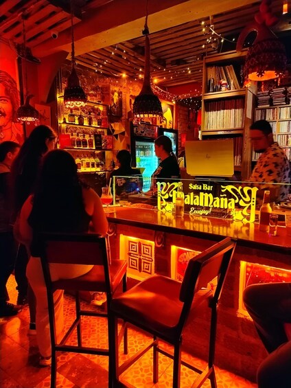 A bar with a sign reading 'Salsa Bar,' people sitting and standing, and shelves with bottles. 1