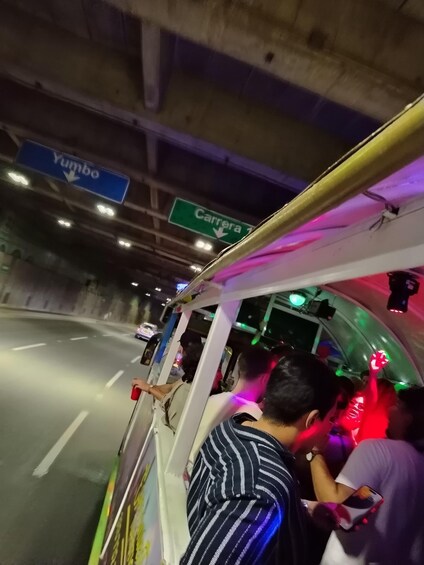 A bus with passengers, overhead road signs, and a road under a bridge. 3
