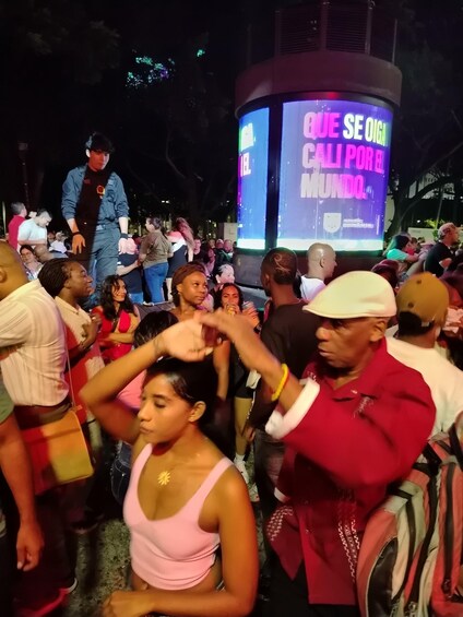 A crowded outdoor event with a large digital screen displaying text. 4