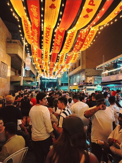 A crowded street with people gathered, illuminated by string lights and banners. 2