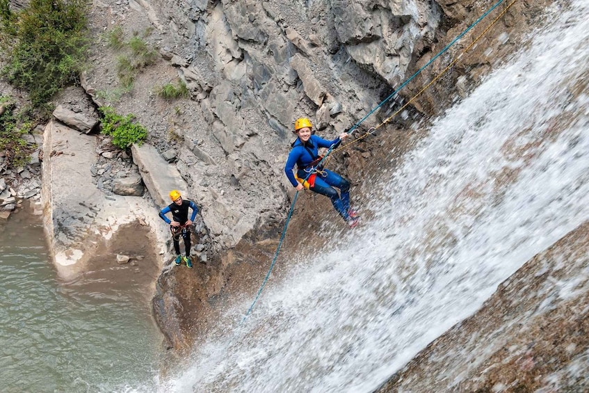 Two individuals rappelling down a rocky waterfall. 2