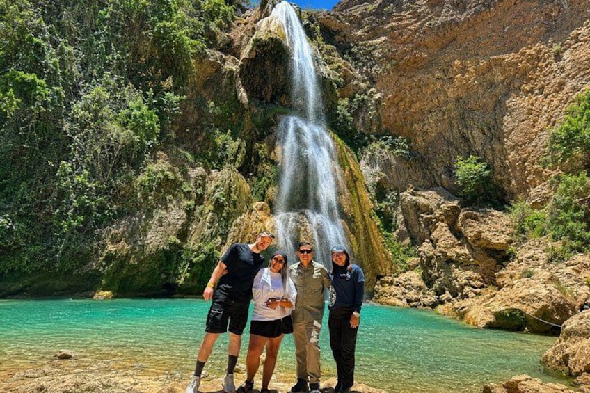 Un grupo de personas de pie junto a una cascada en un cañón rocoso con agua turquesa cristalina. 3