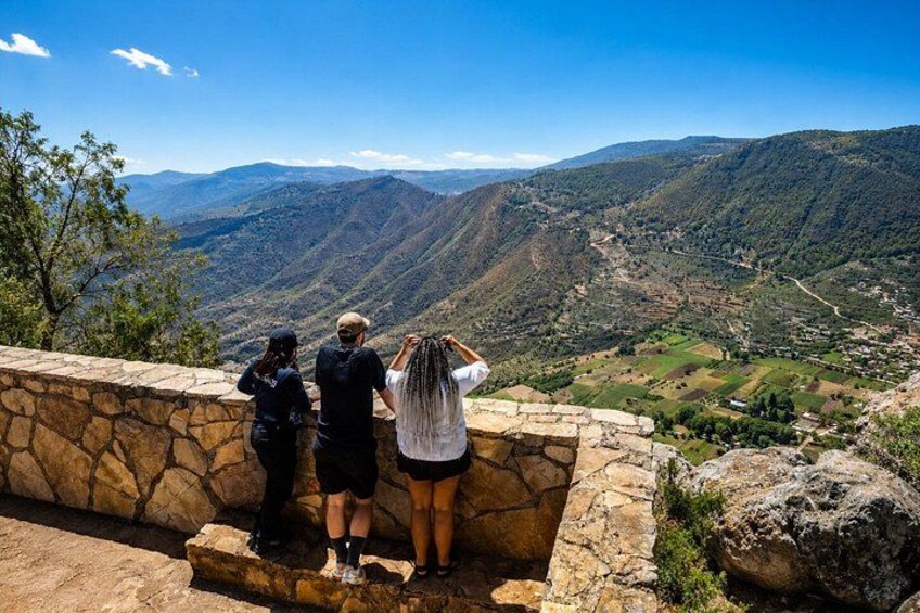 Tres personas de pie sobre un muro de piedra, con vista a un valle y montañas en la distancia. 2