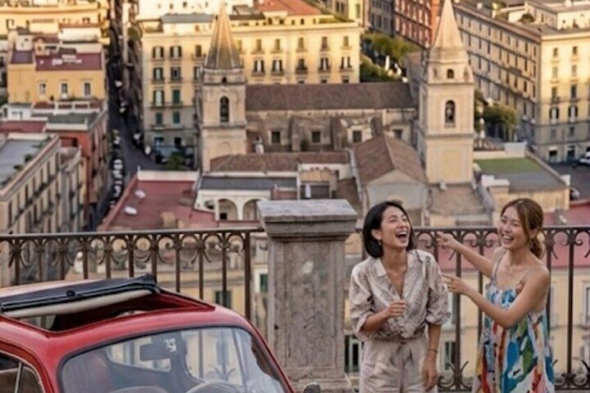 Une voiture rouge est garée sur un balcon, avec une vue sur la ville en arri ère-plan. 4